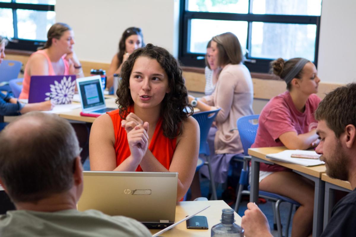 Student in red shirt speaking in front of computer