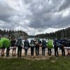 The group of thirteen participants stand with their backpacks on and back to the camera as they raise their trekking poles in excitement over a successful trip. They are positioned along the shore of a beautiful lake in the Sierra Nevada.  