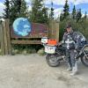 Gasta stands tall in front of a sign along the Dalton highway, noting his arrival at the edge of the Arctic Circle by motorbike with pride.  